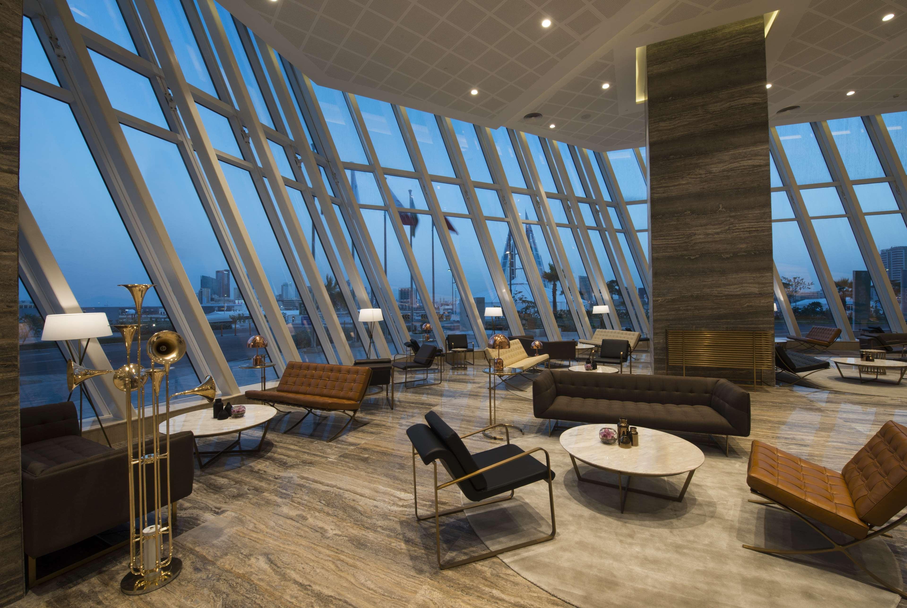 Wyndham Grand Manama Hotel Exterior photo The photo shows a modern lounge or lobby area with a striking architectural design. The space features large windows with a panoramic view, allowing plenty of natural light to fill the room. The interior includes stylish furniture, such as sleek sofa