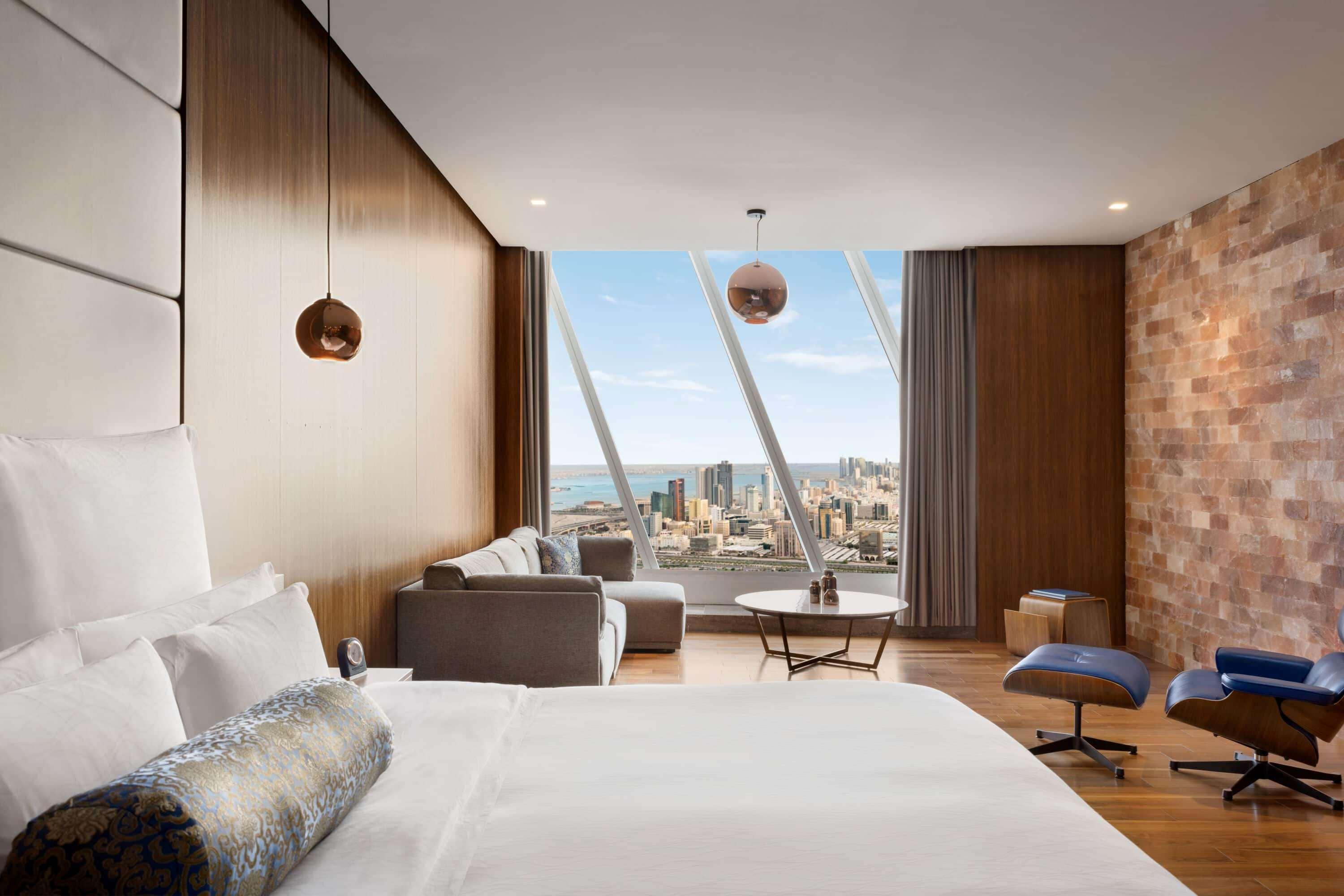 Wyndham Grand Manama Hotel Exterior photo The photo shows a modern hotel room with a stylish interior. The room features a large bed with white bedding and decorative pillows. To one side, there is a comfortable seating area that includes a gray sofa, a round coffee table, and a couple of bl