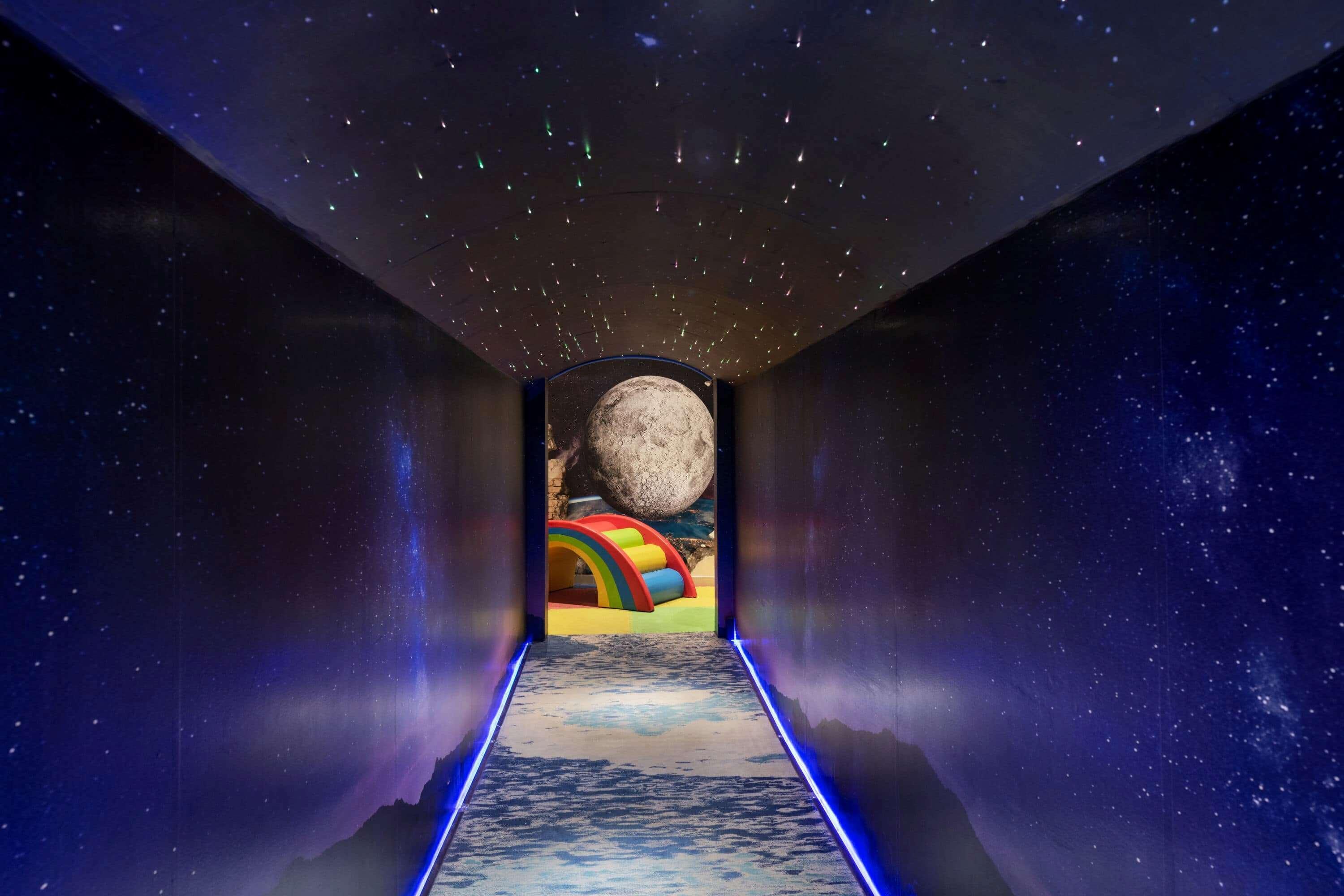 Wyndham Grand Manama Hotel Exterior photo The image depicts a long, narrow hallway that appears to lead into a cosmic space. The ceiling is adorned with a starry sky, while the walls are dark, enhancing the feeling of being in a vast universe. In the distance, there is a large moon visible t