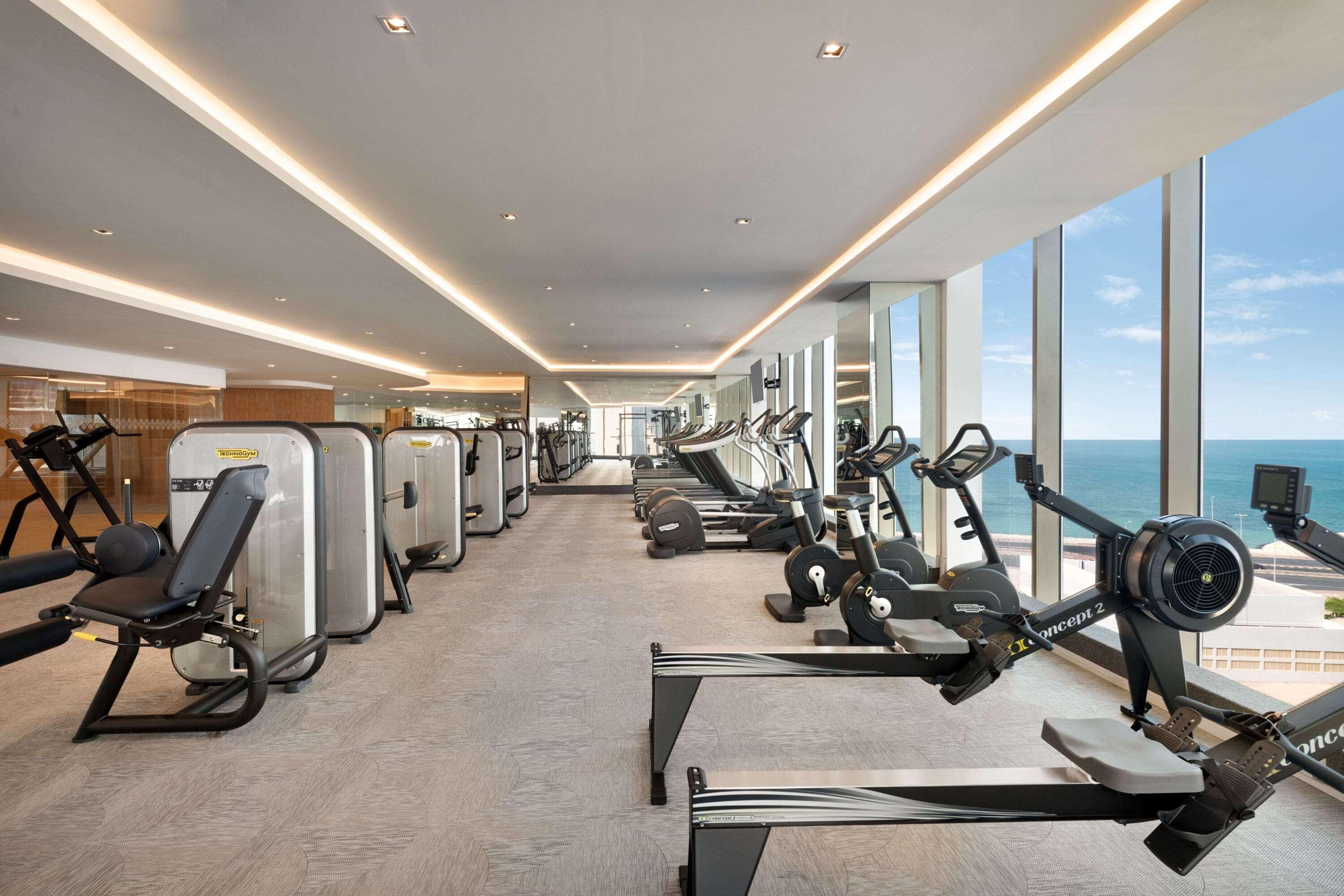 Wyndham Grand Manama Hotel Exterior photo The photo shows a modern gym with a clean and spacious layout. Various exercise machines are arranged throughout the room, including weight machines, treadmills, and stationary bikes. Large windows provide a view of the outside, likely overlooking a 