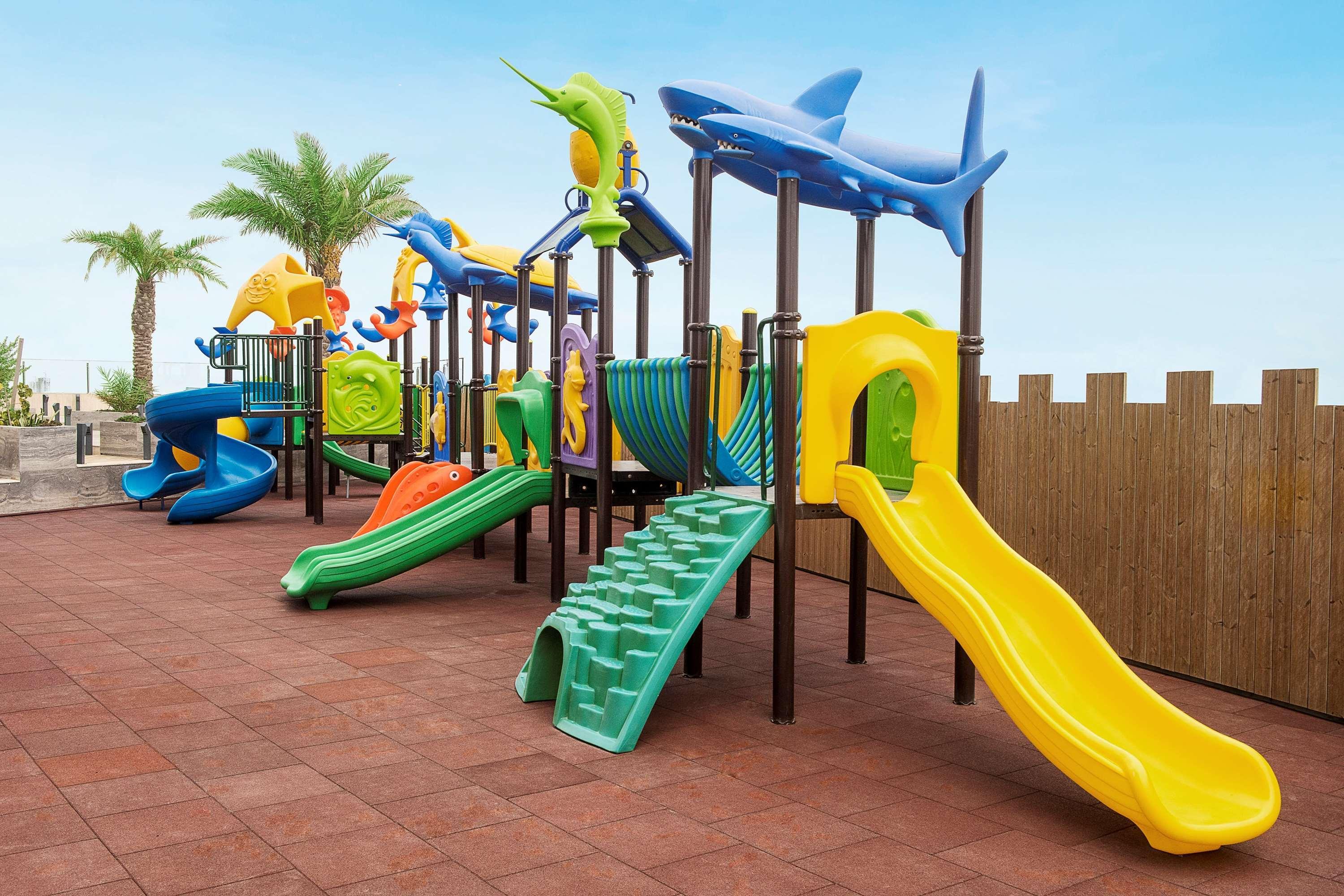 Wyndham Grand Manama Hotel Exterior photo The image shows a colorful playground designed for children. It features various play structures, including multiple slides in different colors, climbing frames, and tunnels. There are also playful designs, such as sea creatures, adorning the playgro