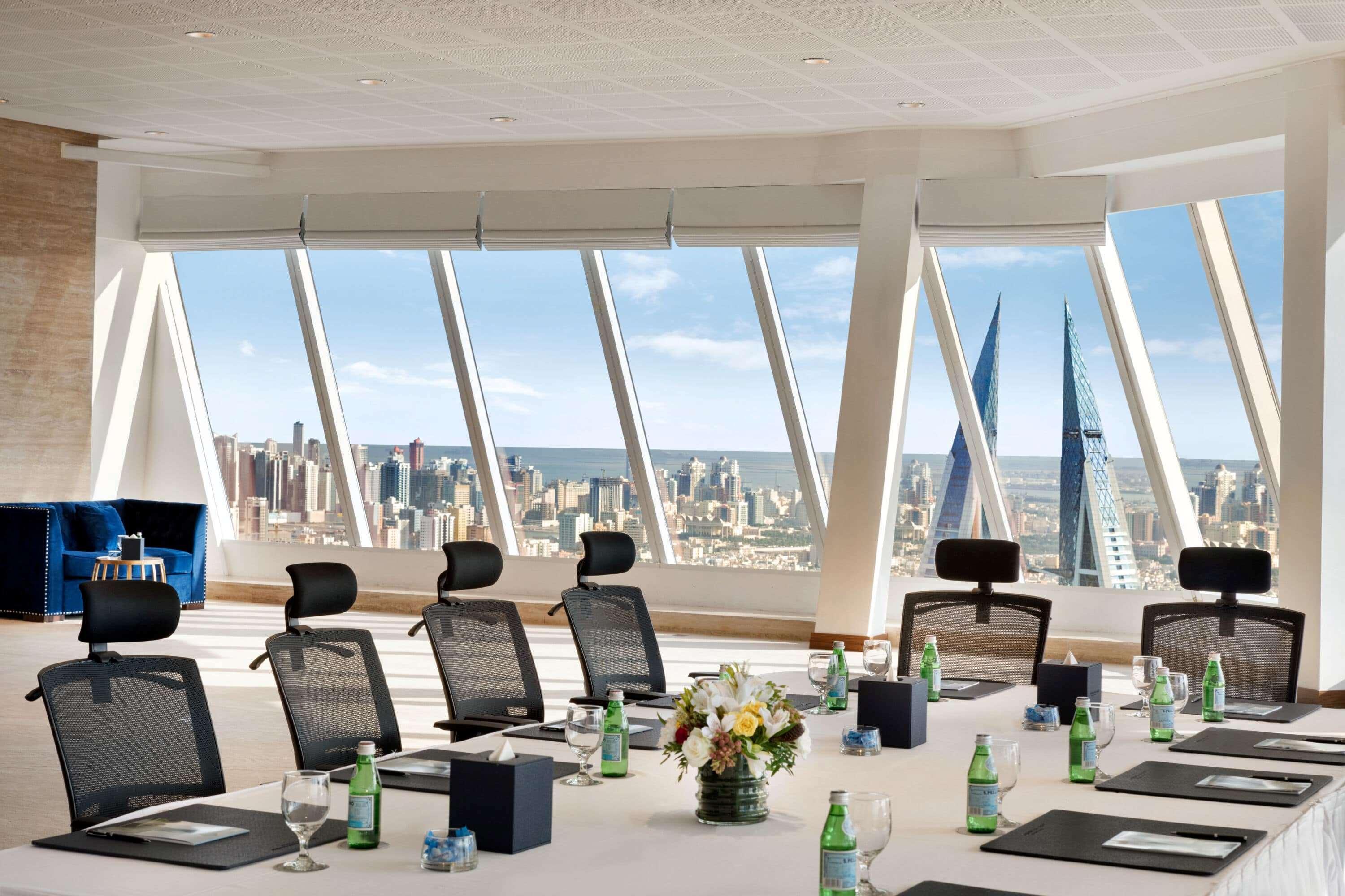 Wyndham Grand Manama Hotel Exterior photo The photo shows a modern conference room with a large rectangular table set for a meeting. The table is adorned with notepads and small bottles of water, along with a floral arrangement at the center. There are several ergonomic black chairs around t