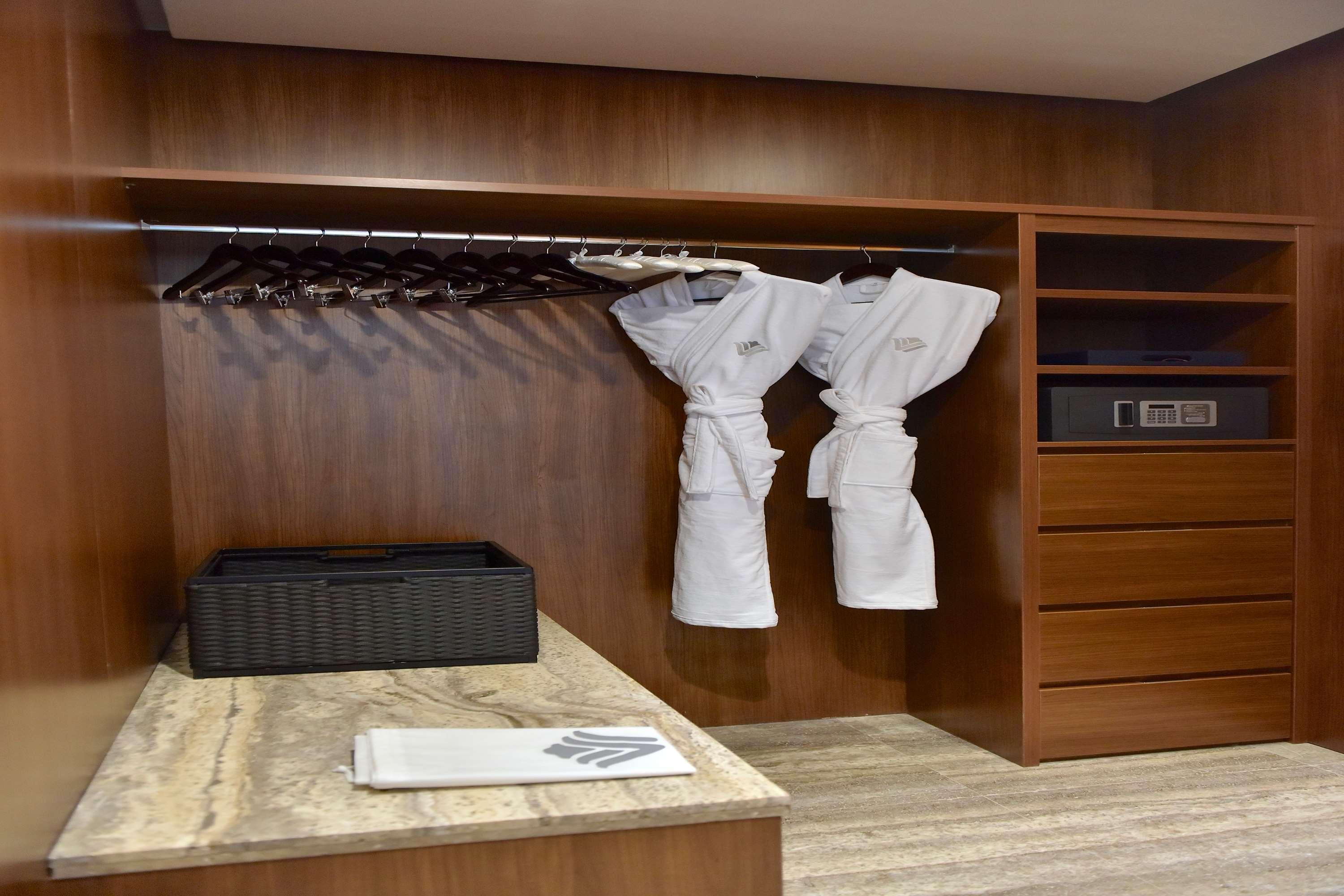 Wyndham Grand Manama Hotel Exterior photo The photo shows a neatly organized closet space featuring wooden walls and shelves. Inside, there are two white bathrobes hanging on a rack. Below the rack, there's a dark woven basket and a small stack of towels or linens. To the right, there's a dr